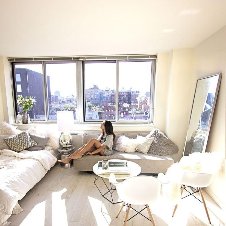 a woman sitting on a couch in a studio apartment with a large window